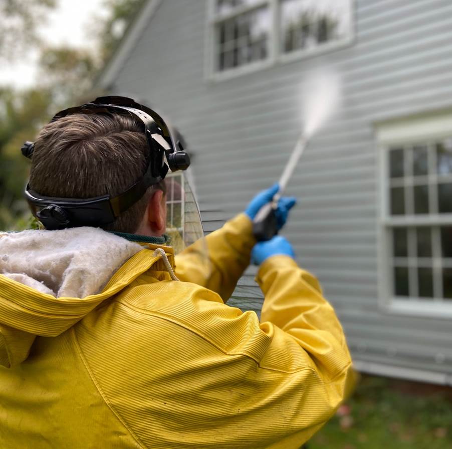 A professional power-washing the exterior of a house